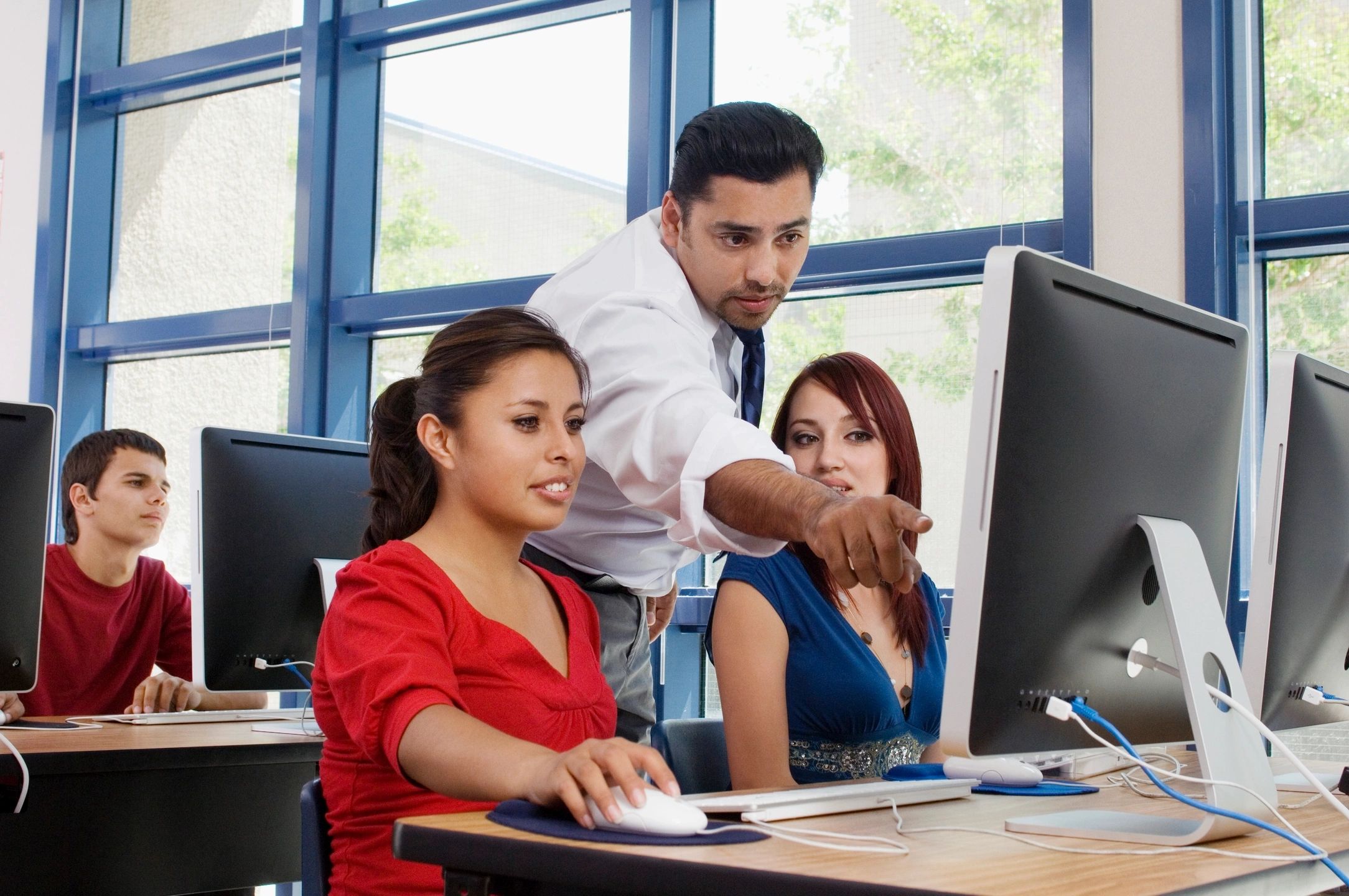 A man pointing at a monitor instructing two students