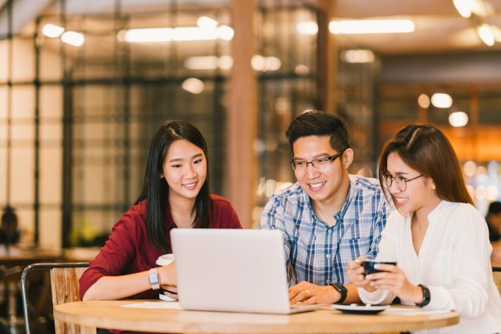 Three people sitting at a table looking at a laptop