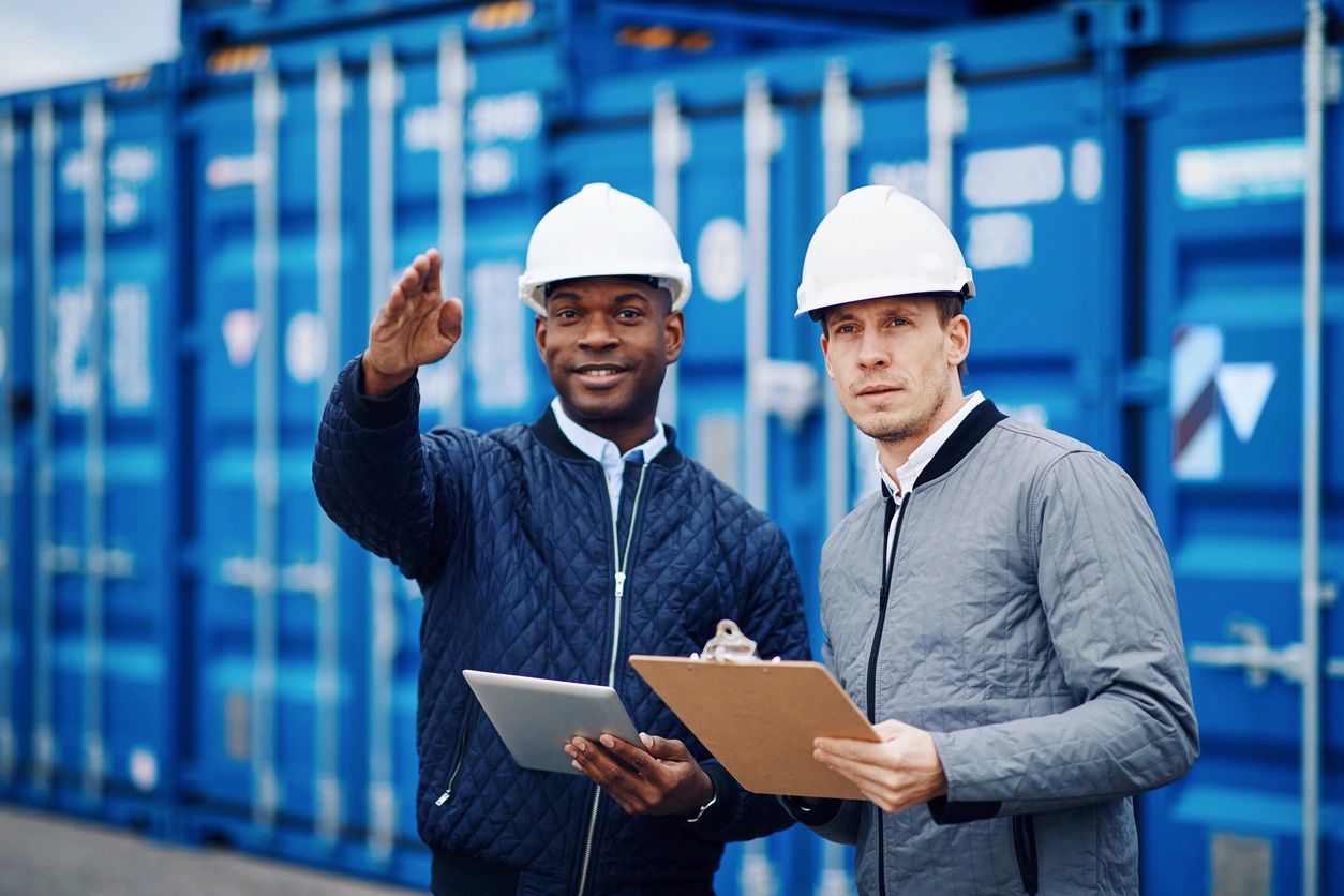 Two men in hard hats next to large storage container