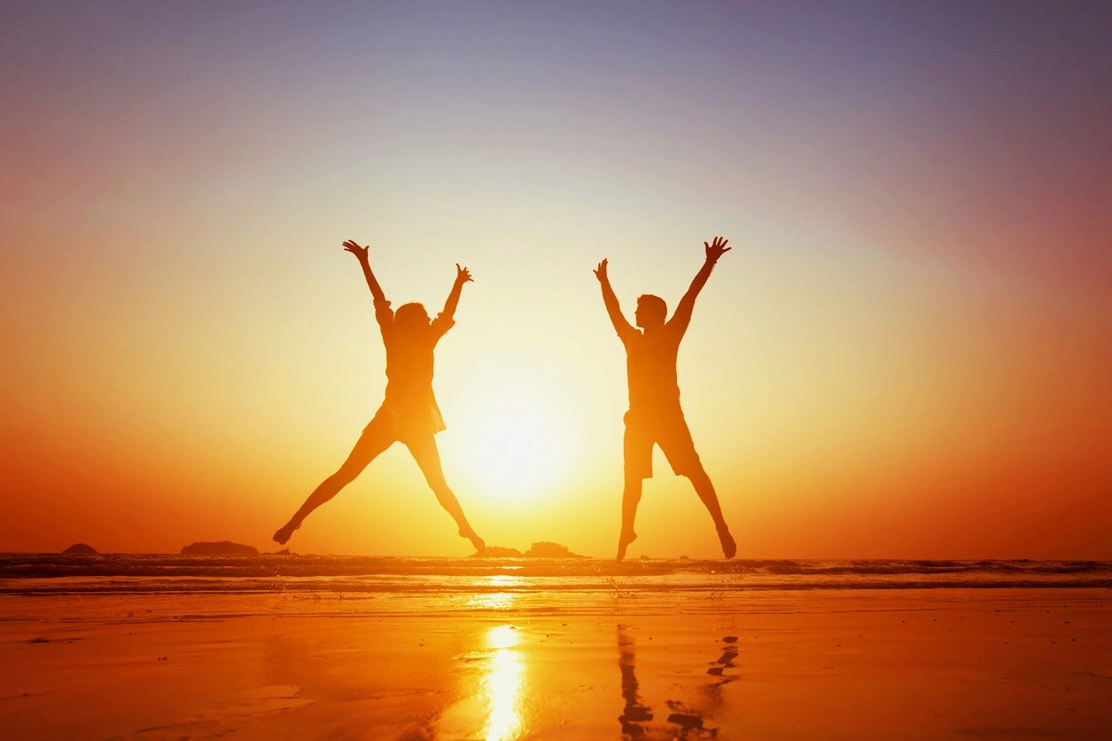 two people in silhouette on a beach jumping 