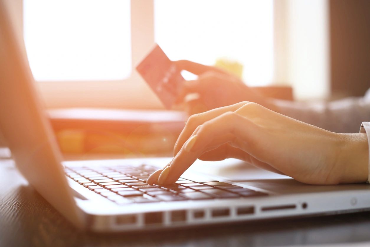 hand typing on keyboard and holding bank card in another